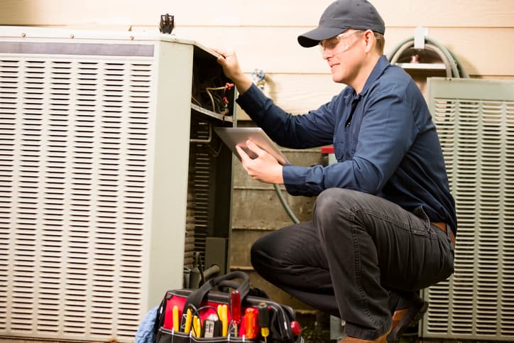 HVAC technician servicing a condenser unit with tablet